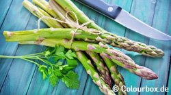 Grüner Spargel und ein Messer liegen auf einem Holztisch