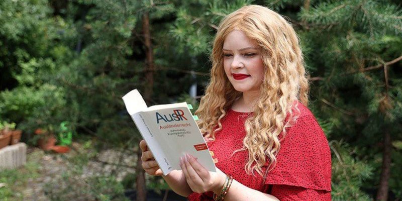 Judith Spangenberg in einem Garten, sie liest in einem Buch mit dem Titel Ausländerrecht