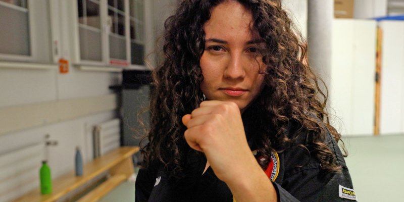 Aylin Çaka mit langen dunklen Locken in einem Trainingsraum, sie ballt die Fäuste zum Kampf 