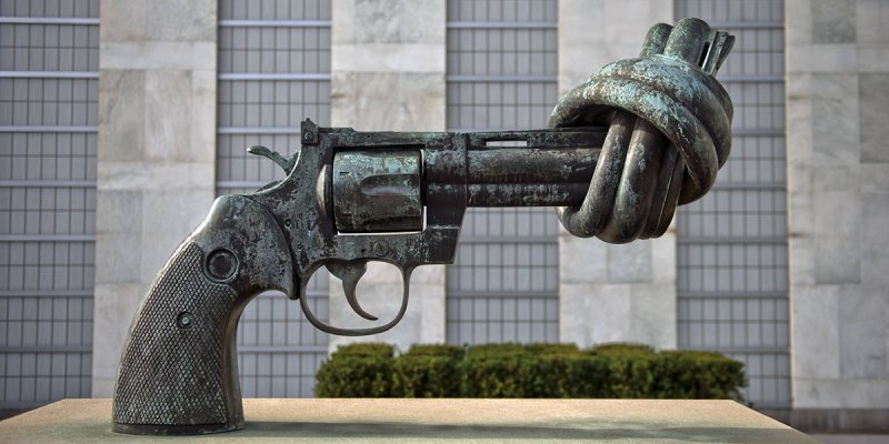 Kunstwerk, das eine Pistole mit eiem Knoten im Lauf darstellt, vor einem Hochhaus der Vereinten Nationen