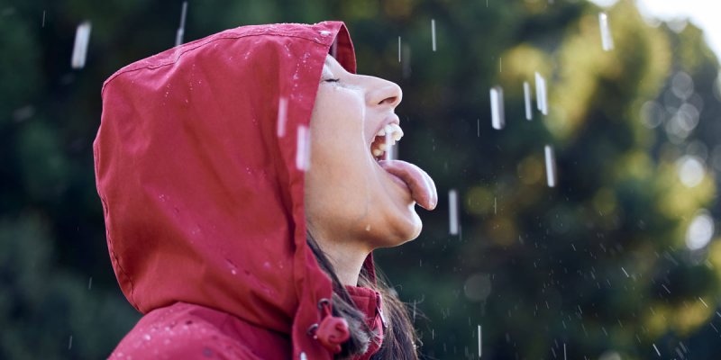 Frau mit Kapuze im Regen, die mit ihrer Zunge die Regentropfen auffängt