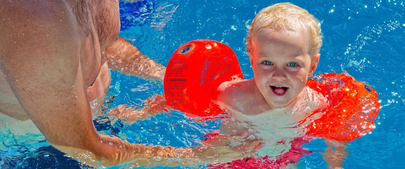 Ein lachendes Kind mit Schwimmflügeln im Wasser