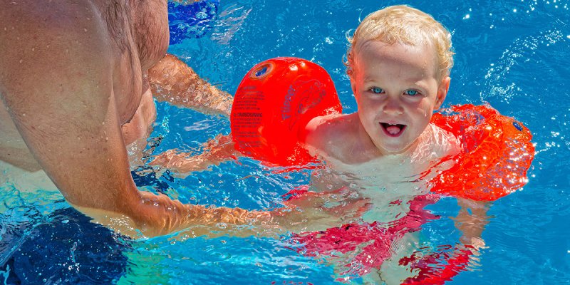 Ein lachendes Kind mit Schwimmflügeln im Wasser